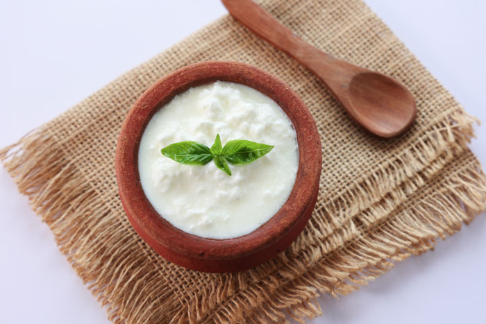 Eine Schale mit cremigem Joghurt, garniert mit frischen Minzblättern, auf einem Naturtuch und einem Holzlöffel daneben.